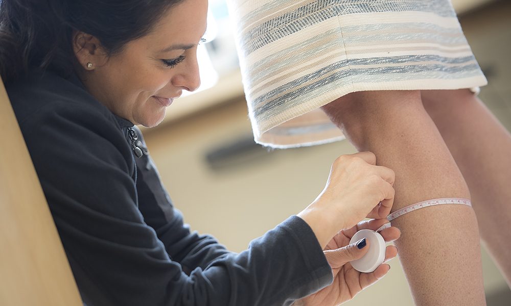 A provider measures the calf diameter of a skirt-clad patient. A provider measures the calf diameter of a skirt-clad patient.